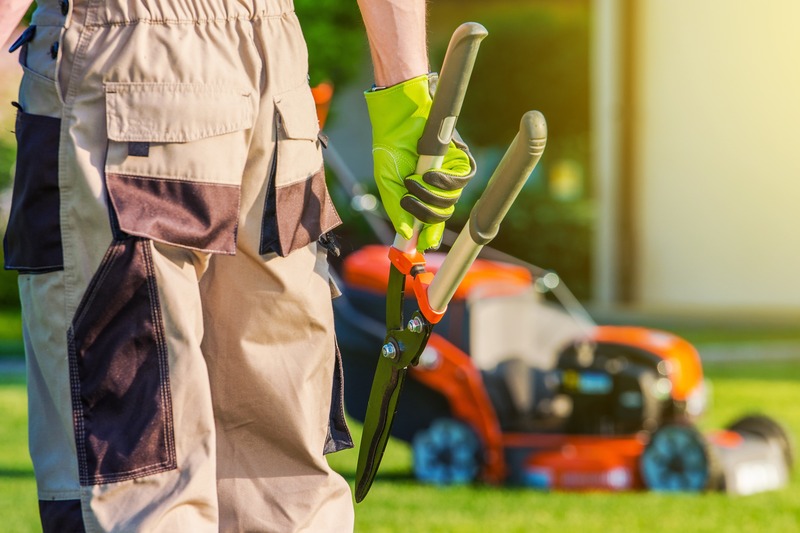A person carries shears toward a lawnmower. 