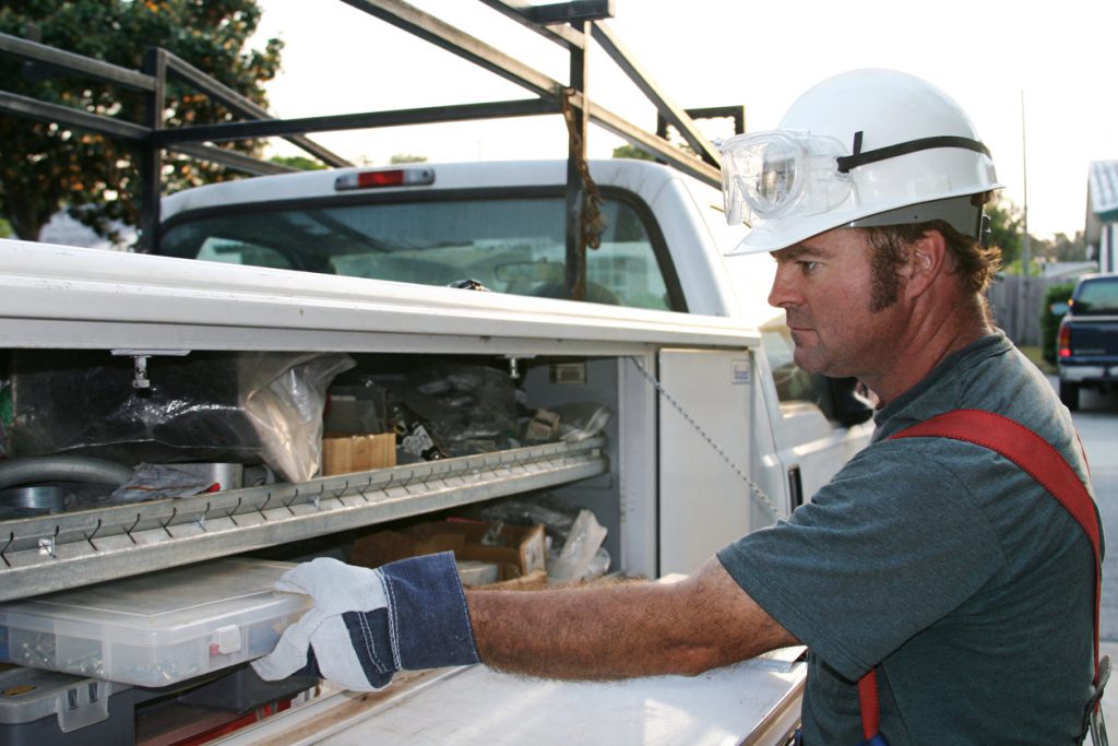 "An electrician reaching onto his service truck, in a suburban neighborhood. Model is a licensed Master Electrician."