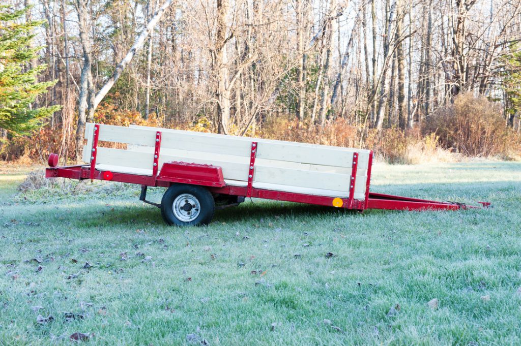 Wooden used utility trailers, red, parked and left in the grass. 