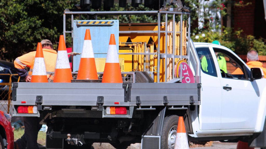 Road work company and service bodies on trucks loaded with signs and orange road cones. Road workers are in the background