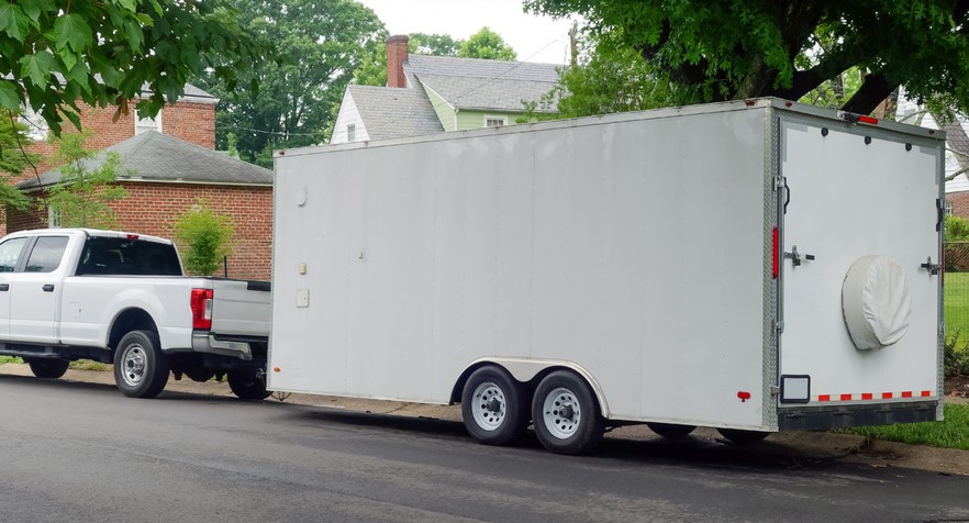 A white truck decides to park a trailer on the side of the road.