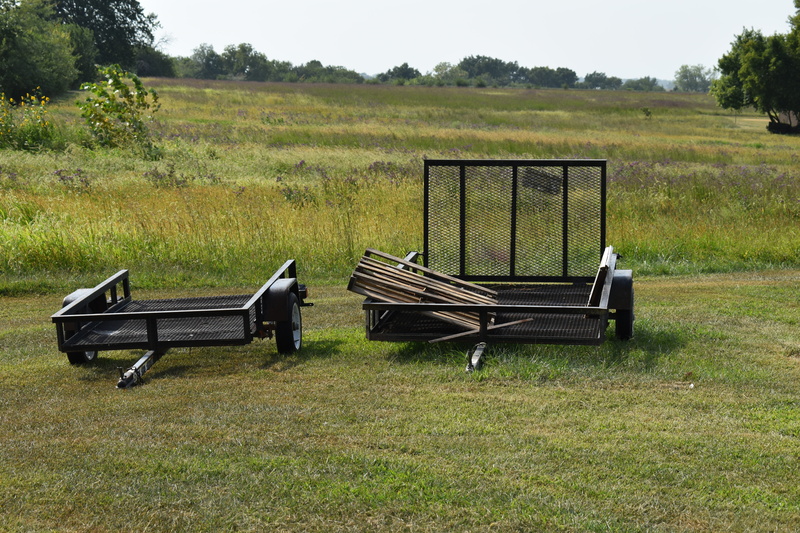 Utility trailers for person use parked in the grass. 