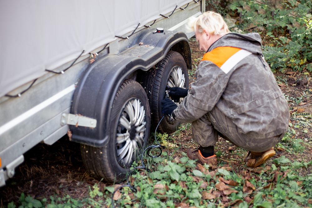 A person performing a home trailer inspection inflates the wheels of a two-axle car trailer with a portable electric air compressor. Service and maintenance of tires.