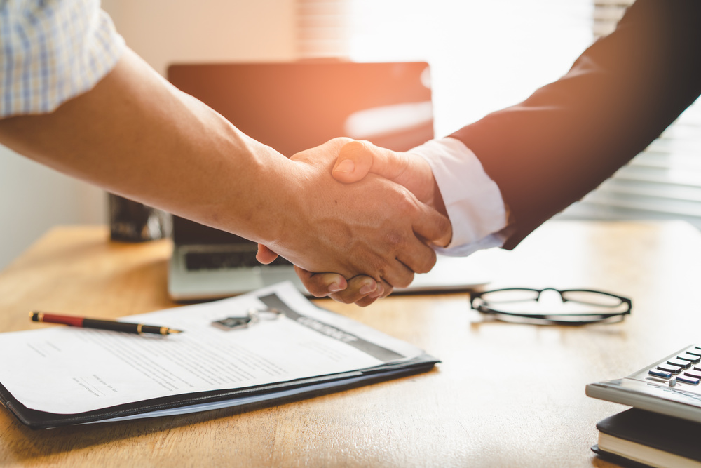 Two people shake hands over a signed contract. 