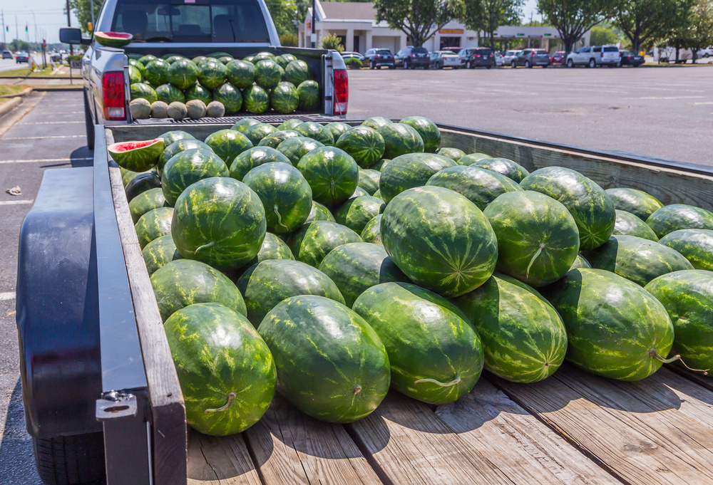 A truck and trailer full of watermelons parked outside a shopping center. 