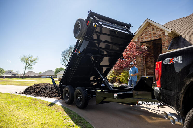 A PJ Trailers dump trailer dumps dirt in front of a house. 