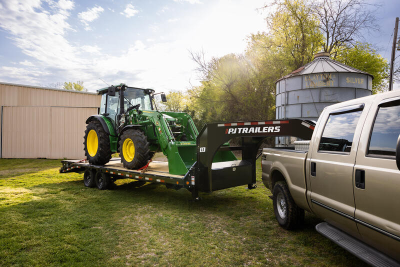 A gooseneck trailer tows a tractor.