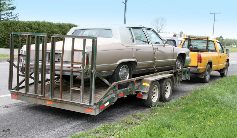 Cadillac on a flatbed and towed by yellow truck.