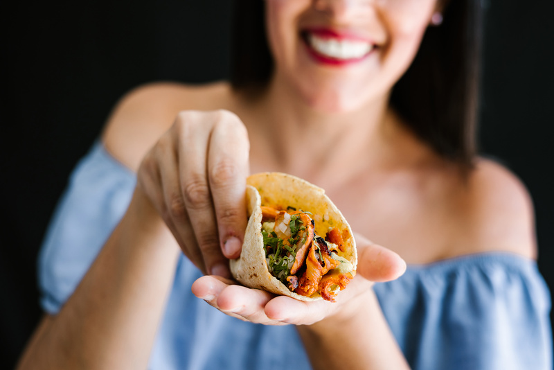 A woman smiles and holds up a taco. 